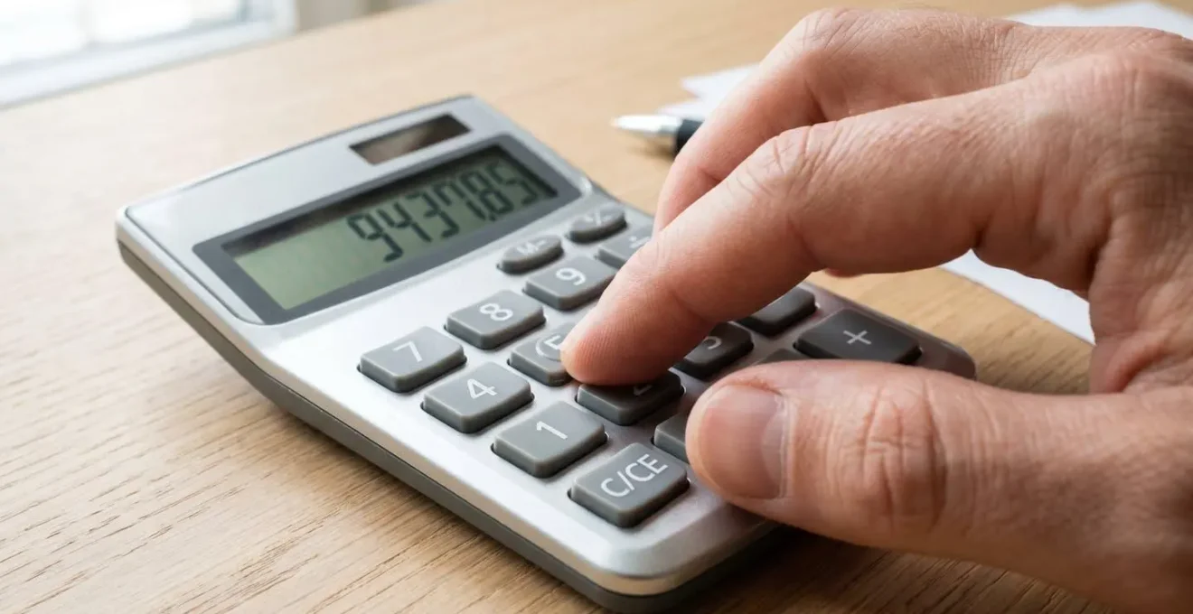 Gros plan sur une main tapant sur une calculatrice posée sur un bureau moderne avec des documents floutés en arrière-plan